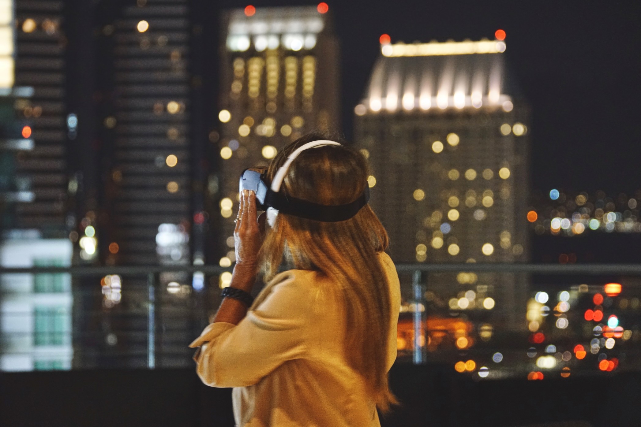 woman-using-virtual-reality-goggles-on-a-rooftop-patio-in-downtown-san-diego-california-at-night-ar_t20_W7EwoL
