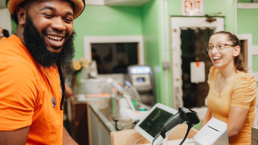 small business owner laughing with customer after managing cash flow to grow business